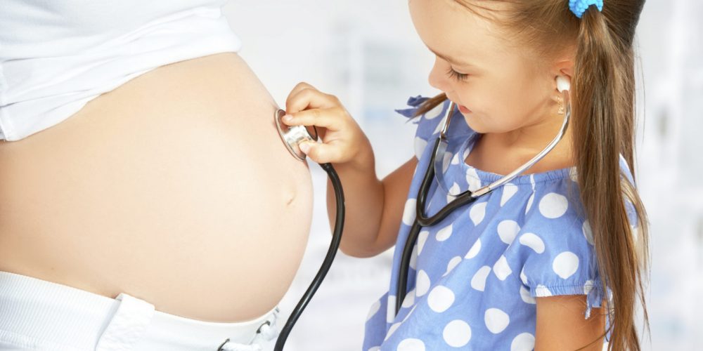 happy family and pregnancy. daughter playing doctor stethoscope and listens to her mother's pregnant belly