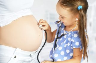 happy family and pregnancy. daughter playing doctor stethoscope and listens to her mother's pregnant belly